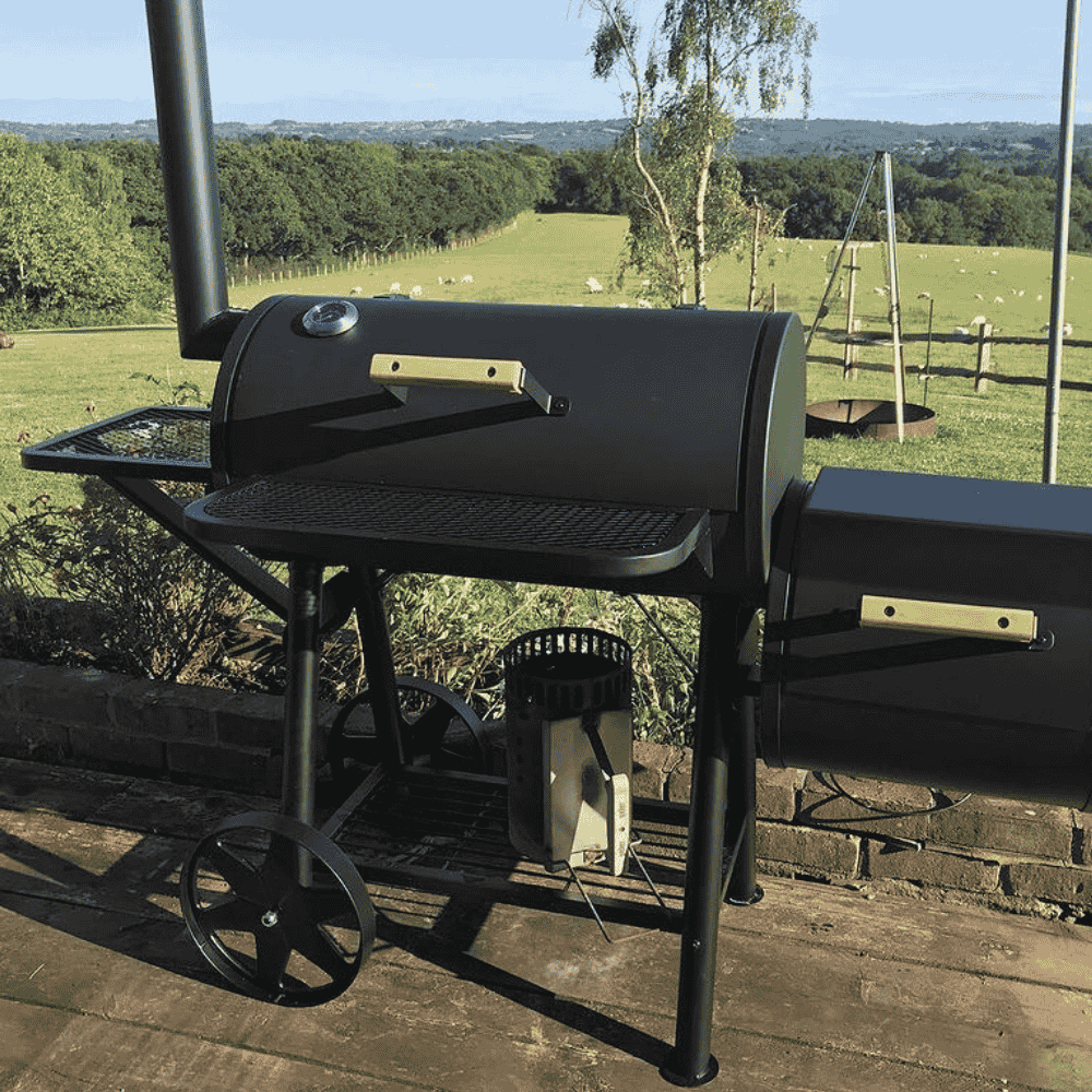 Outdoor setup of large charcoal grill with offset smoker in garden setting